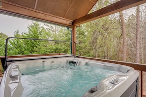 Un jacuzzi con terraza de madera y vistas a un bosque.
