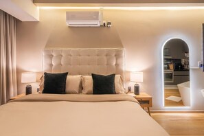 Camera d'albergo con un letto grande, due comodini con lampade, un condizionatore d'aria a parete e vista sulla cucina attraverso un arco.