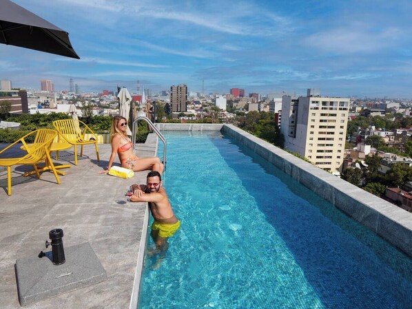 Una piscina sul tetto con acqua cristallina, sedie gialle e vista sulla città sullo sfondo.