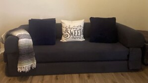 Un canapé de couleur sombre, agrémenté d’un coussin décoratif et d’un plaid.