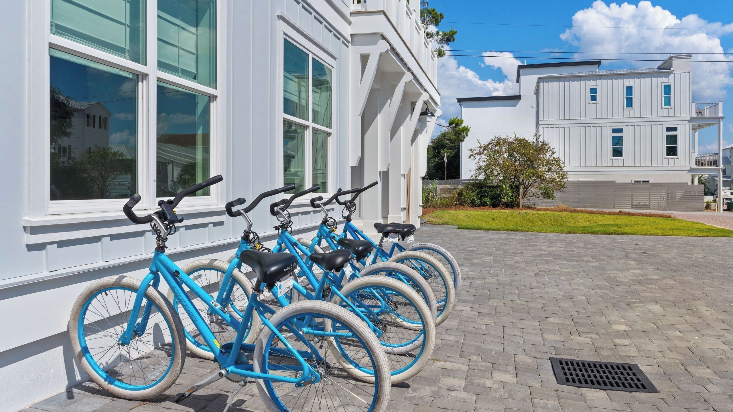 Una fila de bicicletas azules estacionadas frente a un edificio con ventanas grandes y un camino de ladrillos.
