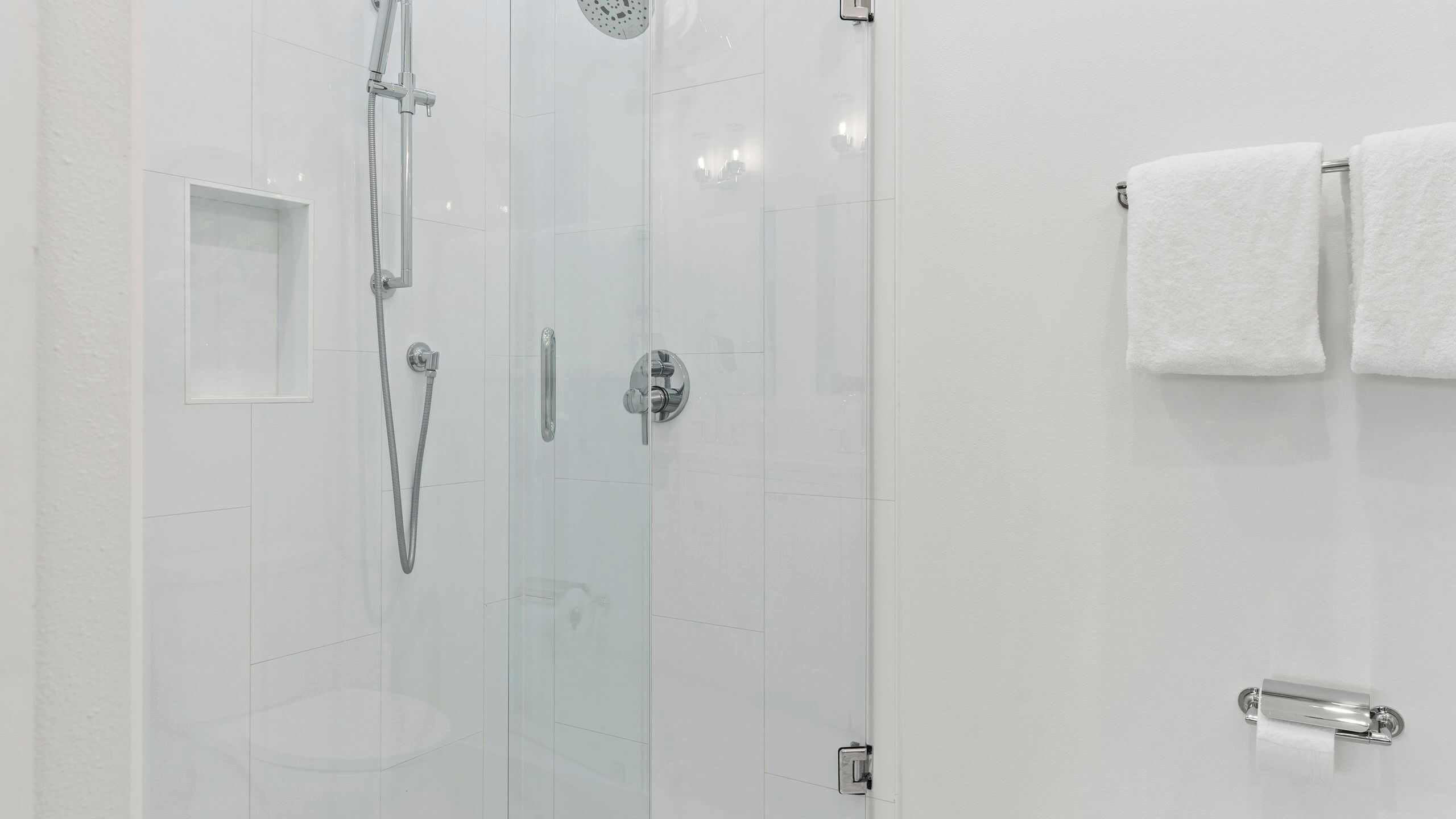 Un baño moderno con cabina de ducha de vidrio, dispensador de papel higiénico y perchero para toallas.