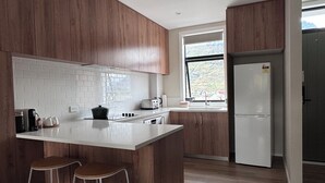 Moderni keittiö, jossa on puukalusteet, valkoinen työtaso ja sisäänrakennettu keittiösaareke, jonka yhteydessä on baarituolit.