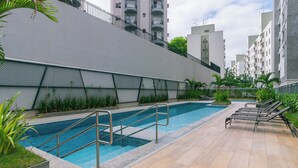 Ein Swimmingpool mit Stufen und Liegestühlen, umgeben von einem Zaun und viel Grün.