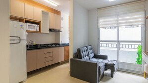 Eine moderne Küche mit integriertem Mikrowellenherd, Herd und Schränken. Im Wohnbereich befindet sich ein graues Sofa und ein kleiner Tisch, sowie eine Glastür, die auf einen Balkon führt.