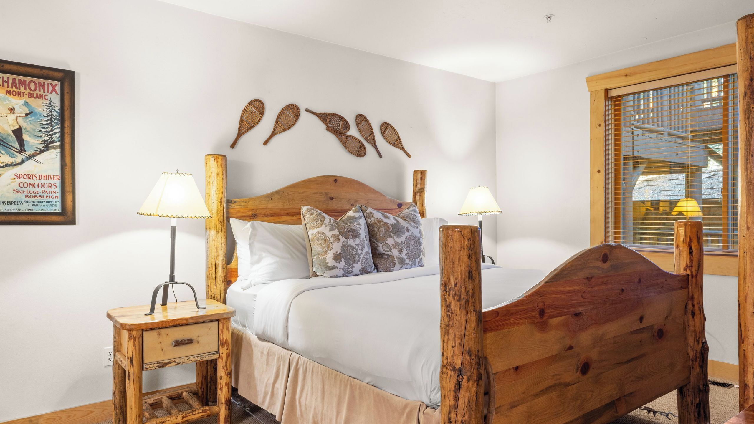 Una cama con cabecera de madera, dos mesitas de noche con lámparas, almohadas estampadas y un póster en la pared.