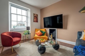 A living room with a red chair, a yellow armchair, a glass coffee table, a television, and a window with a view of buildings. - Cosy Harbour Luxe • Modern 2BR   • Sleeps 6 (Torbay)