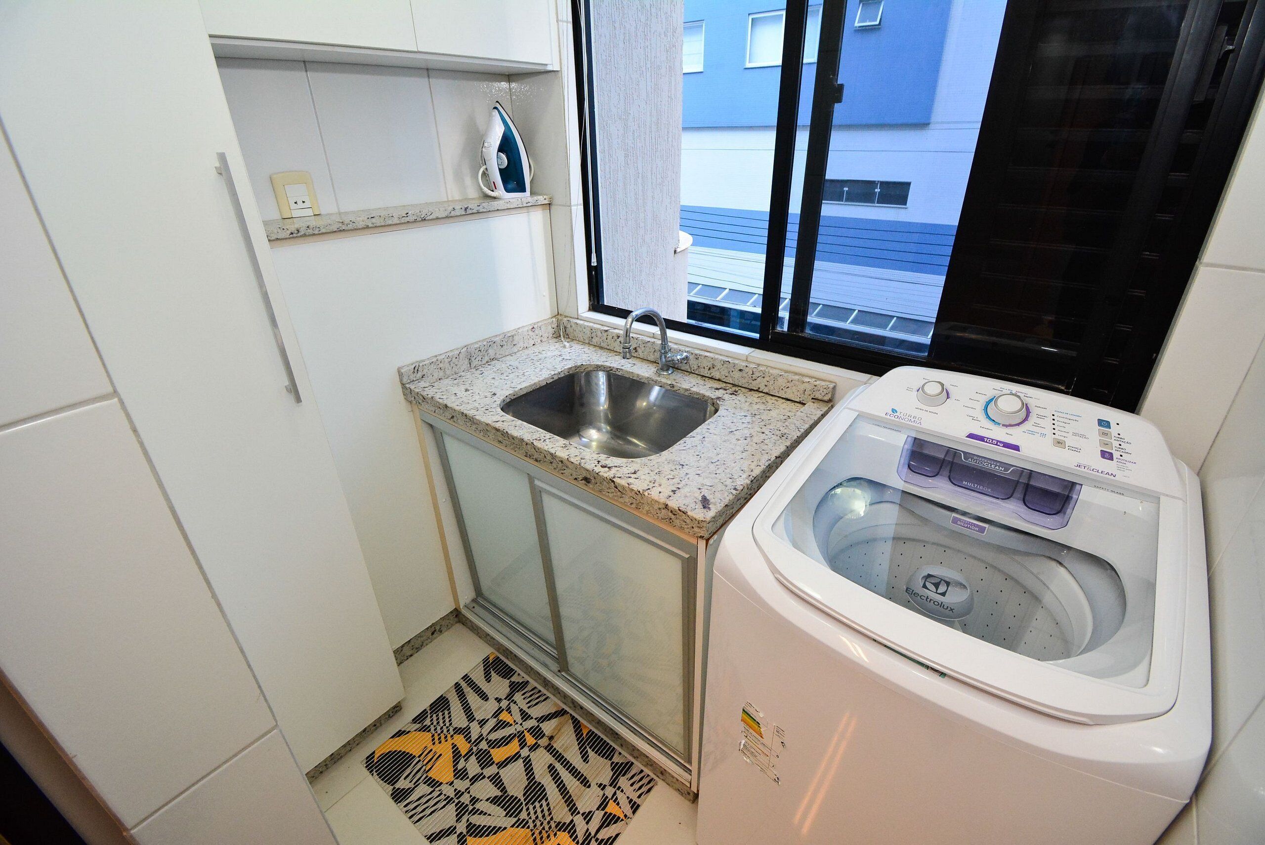 A compact kitchen with a built-in sink, a washing machine, and a window with a view of a building outside.