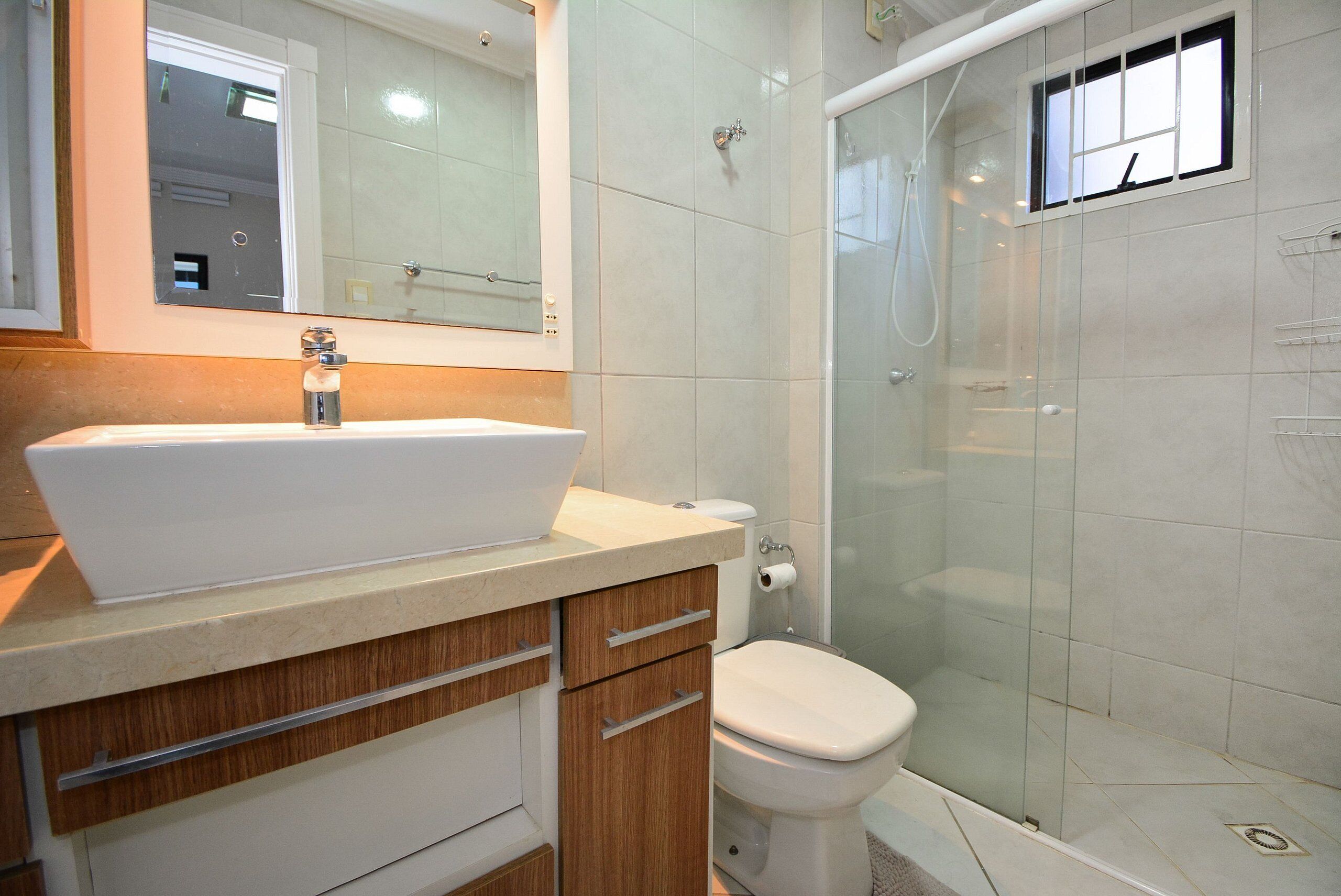 A bathroom with a white sink, wooden cabinets, a toilet, and a glass-enclosed shower.