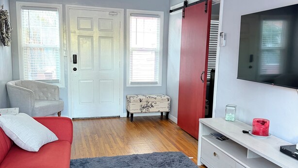 Un salon moderne avec un canapé rouge, un tapis gris, un meuble de rangement blanc et un téléviseur.