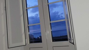 Vue d’un coin de pièce, avec une grande fenêtre, une porte et une vue dégagée sur le ciel.