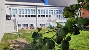 Un immeuble résidentiel à la façade blanche, doté d’un escalier apparent et d’un petit jardin avec de la pelouse et des plantes en pot.