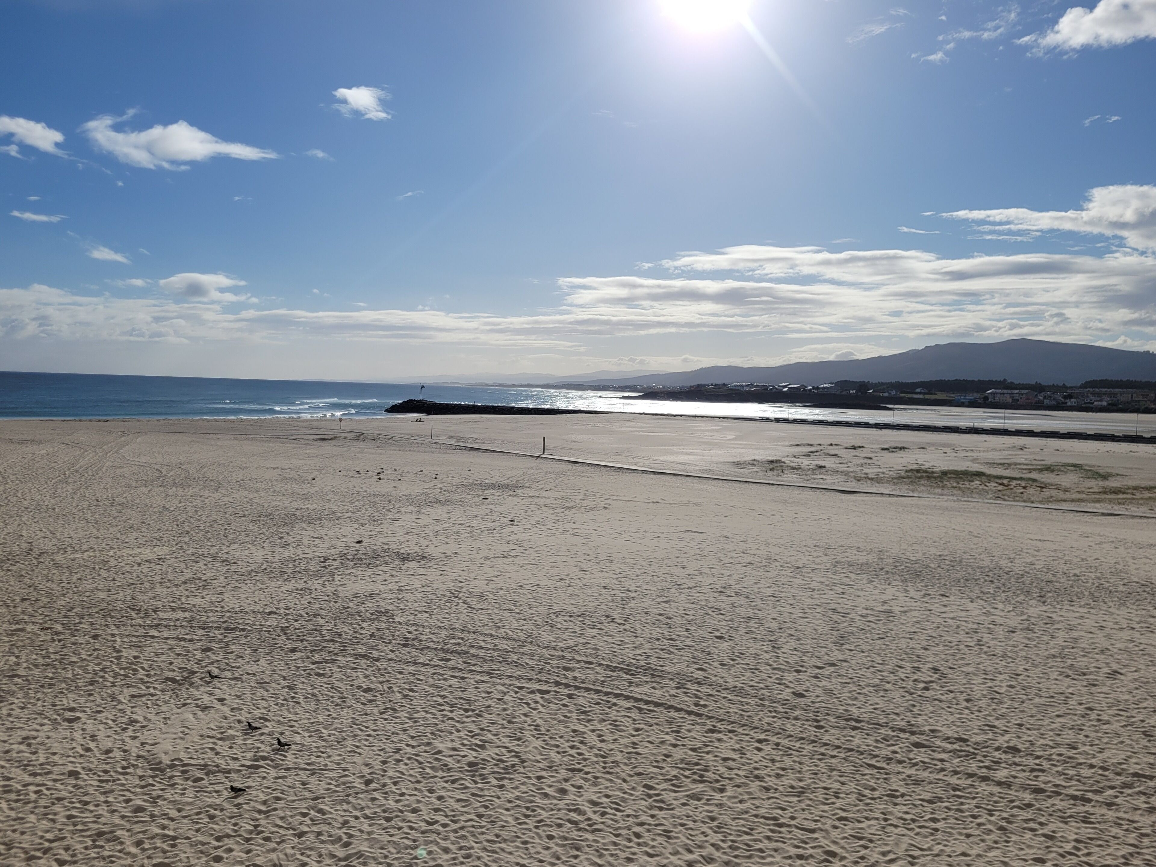 A beach with a clear sky, calm sea, and distant mountains.