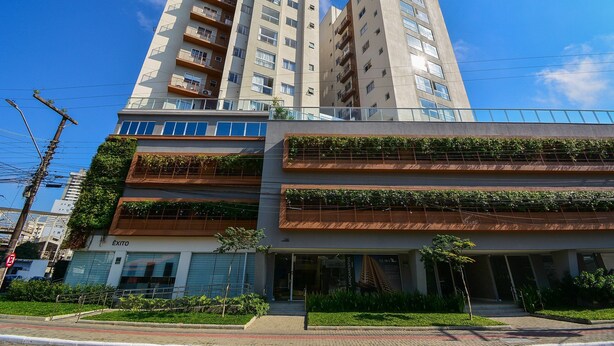 A multi-story building with balconies, a storefront, and a clear blue sky. - Apartamento Aconchegante em Itajaí (Itajaí)