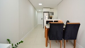 A modern kitchen with white cabinets, a refrigerator, and a microwave. There is a dining table with four chairs and a vase of flowers. - Apartamento Aconchegante em Itajaí (Itajaí)