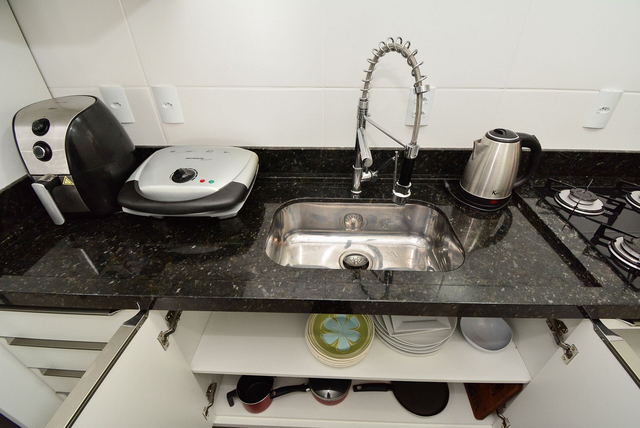 A kitchen with a stainless steel sink, a kettle, a toaster, and a dish rack.