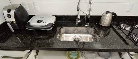 A kitchen with a stainless steel sink, a kettle, a toaster, and a dish rack.