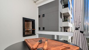 A wooden cutting board with two knives on a black table, a framed picture on the wall, and a view of a building through a window. - Apartamento Aconchegante em Itajaí (Itajaí)