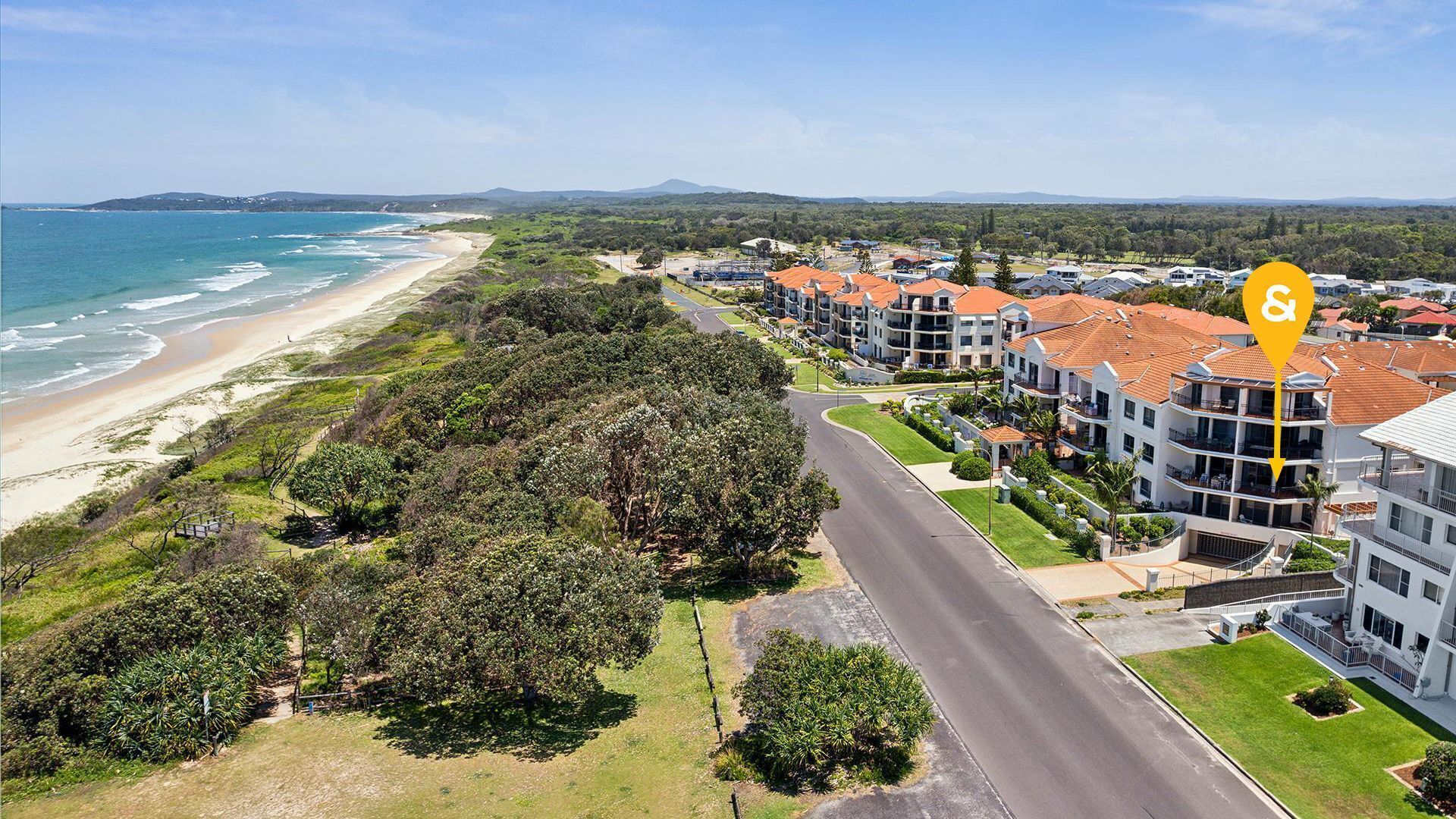 A coastal residential area with beachfront properties, a main road, and a mix of greenery and buildings.