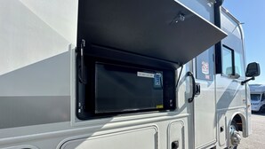 A white RV with a large sliding door, a mounted TV, and a 23-year warranty sign. - 2025 RV with 2 full baths sleeps 9 (Coram)