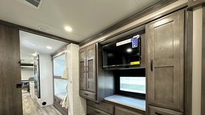 A compact kitchen with built-in appliances, a window with a view, and a small seating area. - 2025 RV with 2 full baths sleeps 9 (Coram)