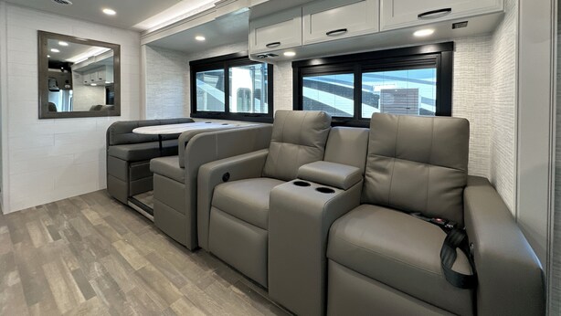 A modern RV interior with a seating area, a small kitchenette, and a large window providing a view of the outside. - 2025 RV with 2 full baths sleeps 9 (Coram)