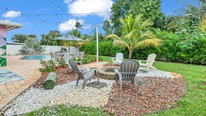 Ein Garten mit Pool, Sitzgelegenheit im Freien und einer Feuerstelle, umgeben von Kies und Pflanzen.