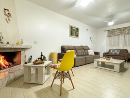 Uma sala de estar com lareira, um sofá, uma poltrona amarela e uma mesa de centro.