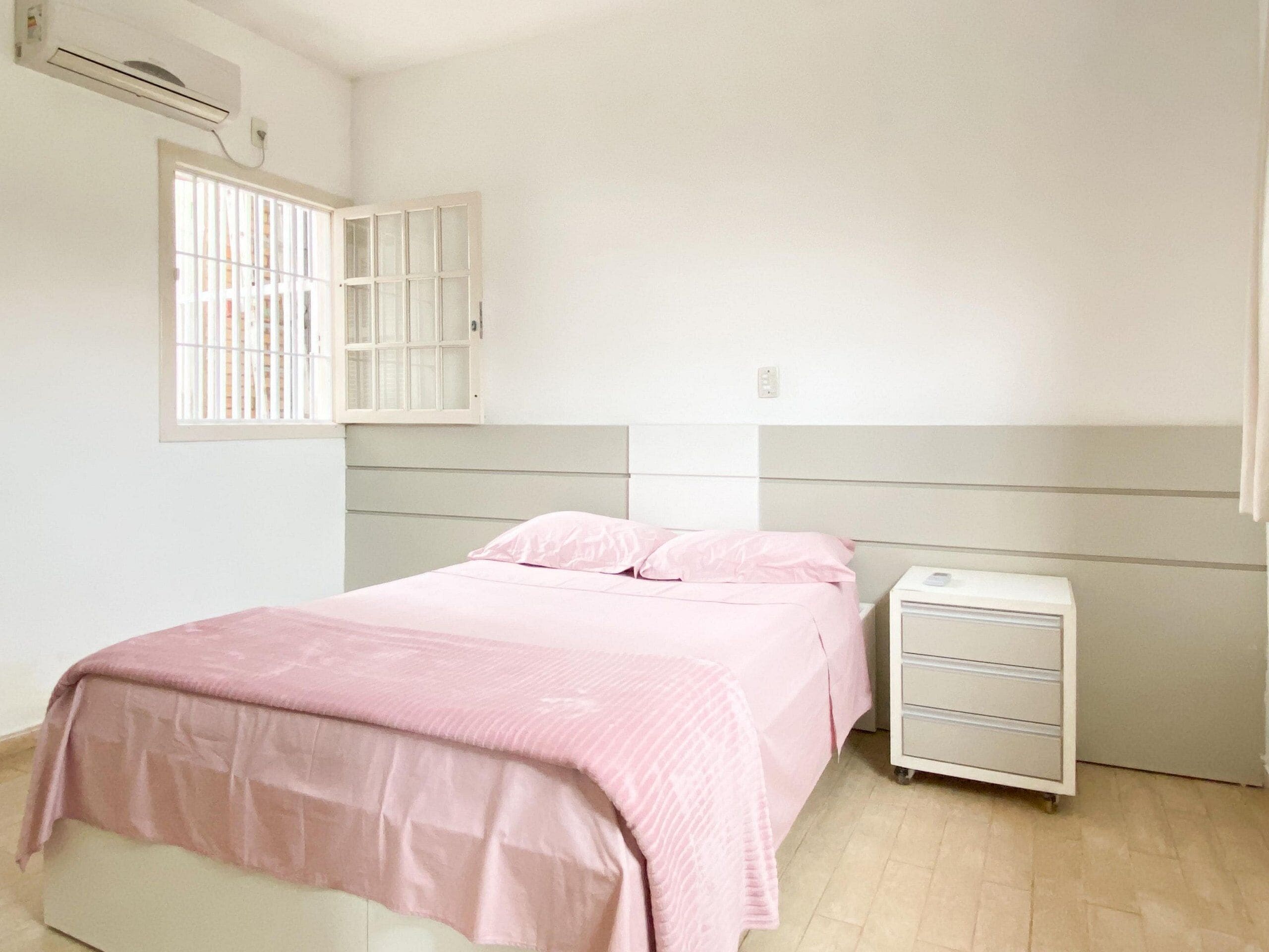 Una camera da letto con un letto, un comodino, una cassettiera, una finestra con sbarre e un condizionatore d'aria.