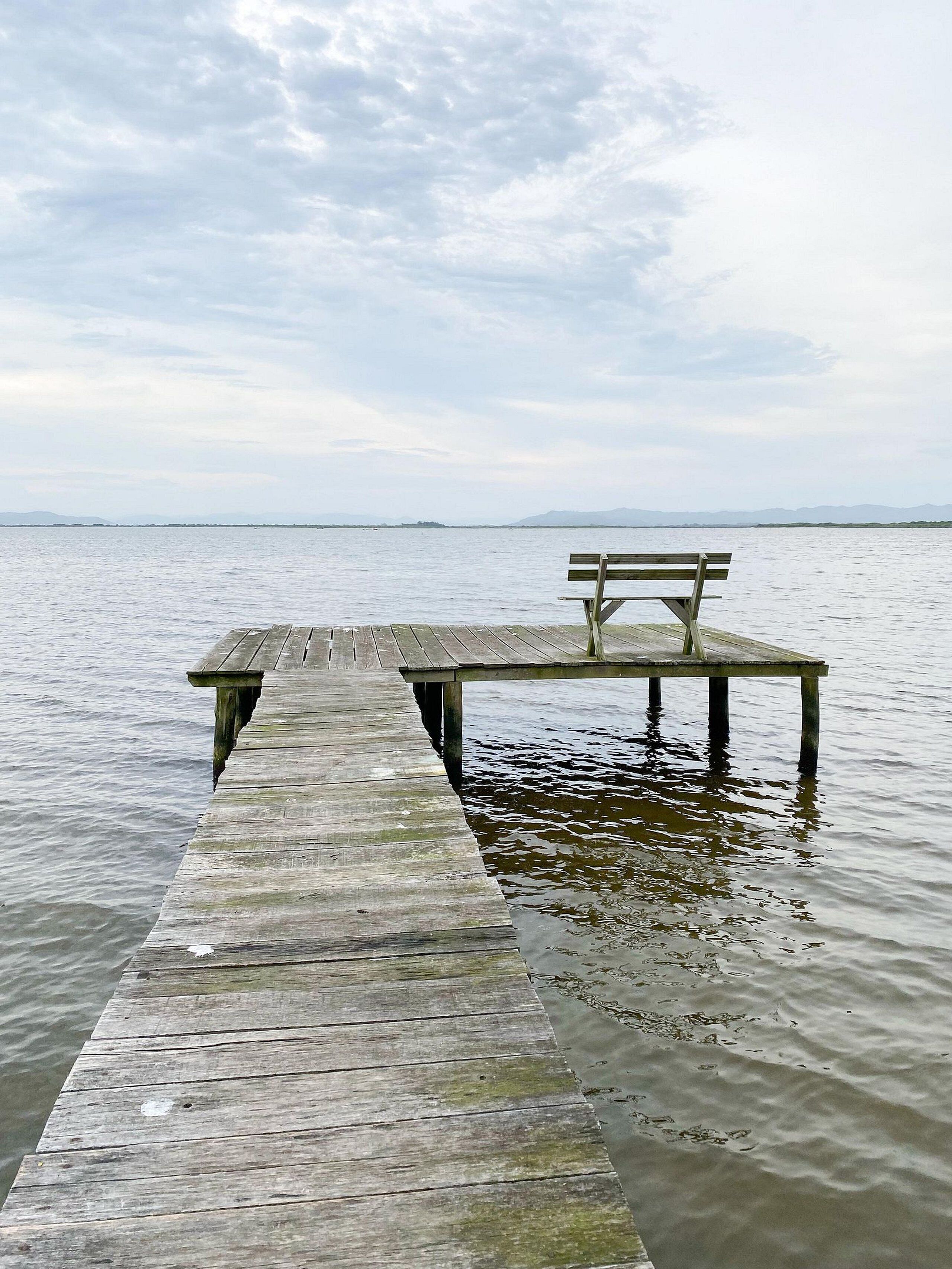 A wooden pier extending into calm water with a bench at the end.