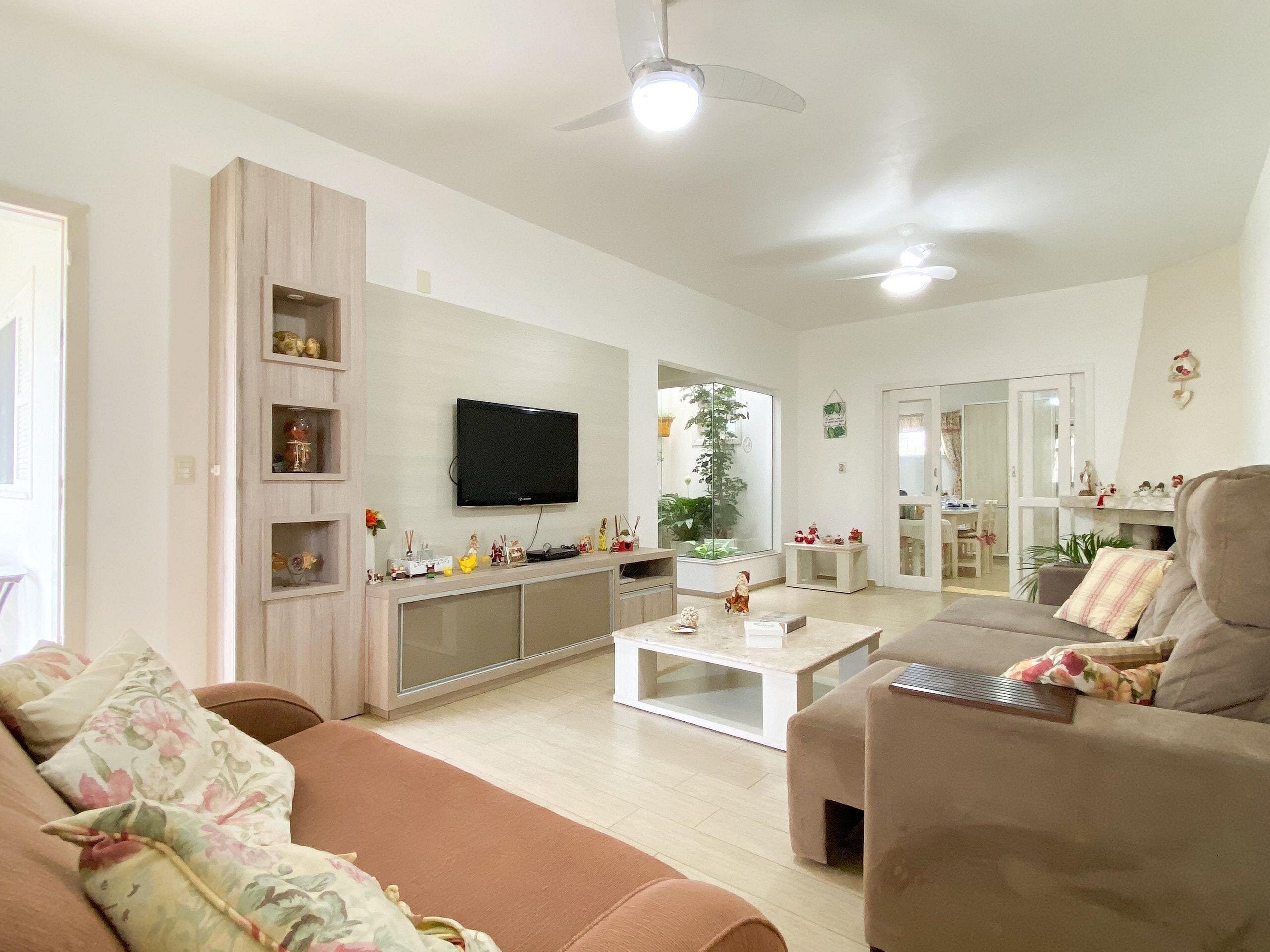 Uma sala de estar espaçosa com televisão de tela plana na parede, uma janela grande e um ventilador de teto.