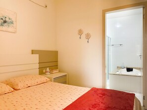 Une chambre à coucher comprenant un lit, une table de chevet, un miroir et une salle de bain avec une douche et un porte-serviettes.