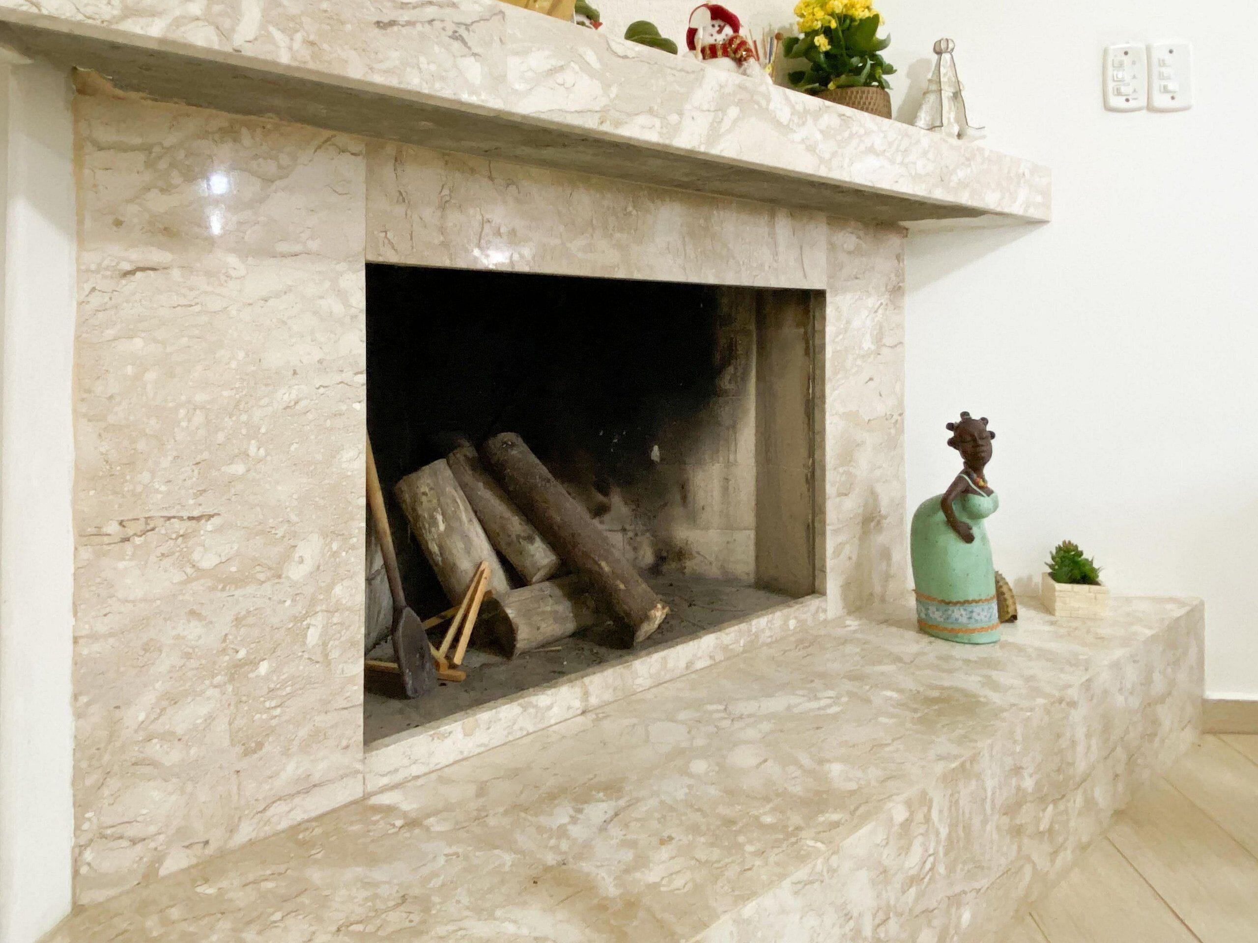 Un camino in marmo con tronchi di legna, una figura decorativa e una piccola pianta sulla mensola.