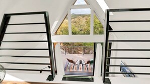 A room with a sloped ceiling, large windows, and a view of a deck with outdoor furniture. - Starrynight Modern Cabin - BRAND NEW! (Wimberley)
