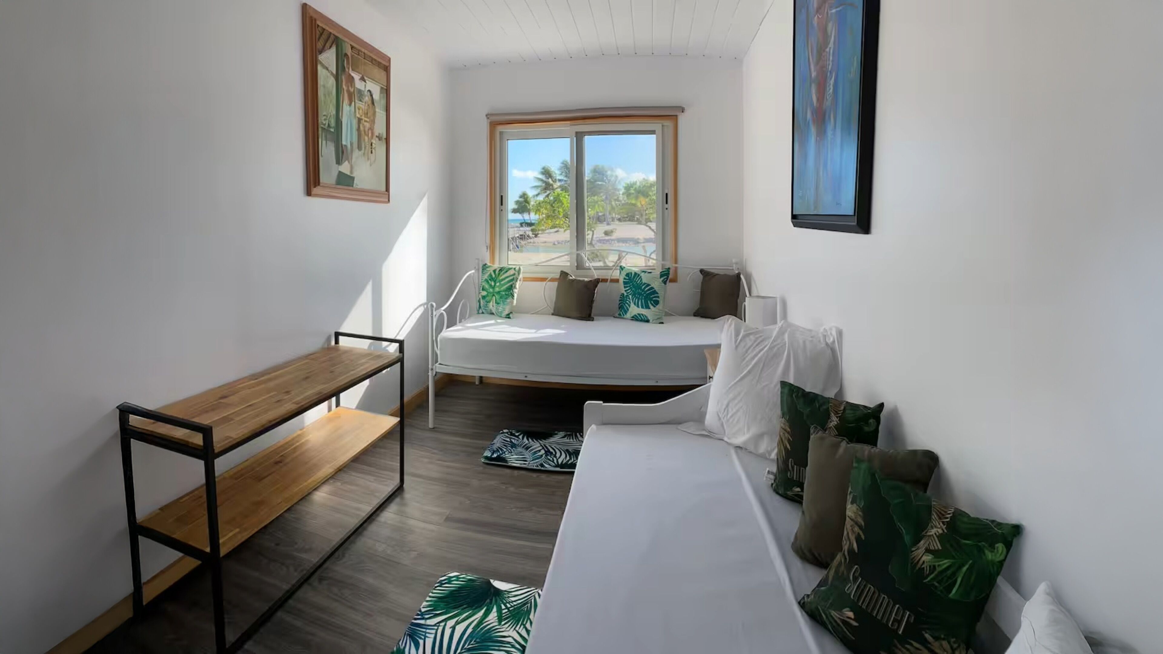 Una habitación pequeña y moderna con una cama, un banco y una ventana con vistas a palmeras.