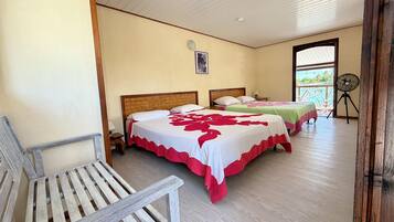 Habitación de hotel con dos camas, una silla de madera, un ventilador y vista al mar.