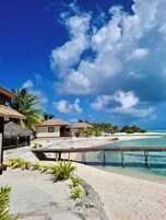 Un resort tropical con bungalós sobre el agua, aguas turquesas cristalinas y una playa de arena.