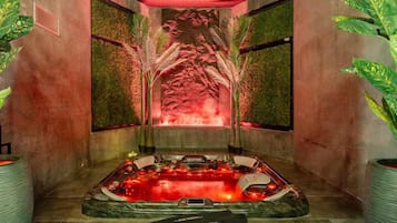 Een spa ruimte met een jacuzzi, een massagetafel en een muur met een abstract rood ontwerp.