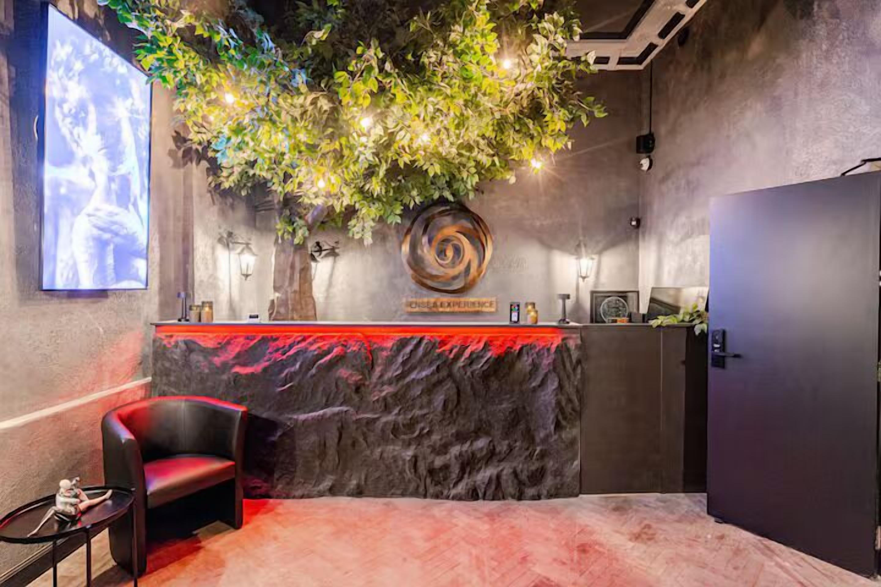 Un área de recepción con mostrador de mármol, un sillón de cuero negro y una televisión instalada en la pared.