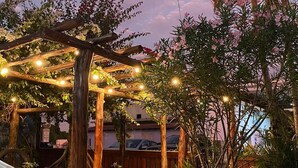 A hammock under a wooden pergola with string lights, surrounded by greenery and a sunset sky. - Pousada Serra Azul: comfort, hospitality and nature for your best experience. (Bom Jardim)
