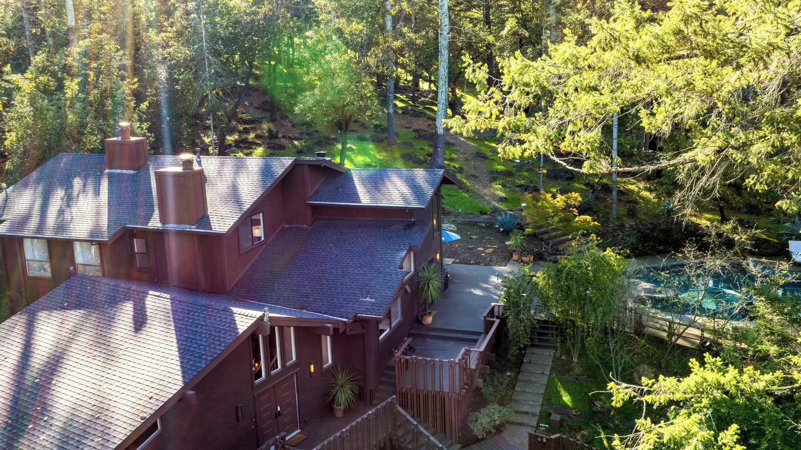 A two-story house with a steeply pitched roof, surrounded by dense forest.