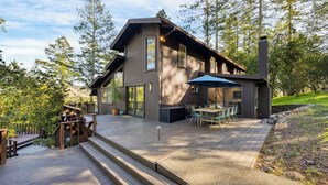 A modern wooden cabin with a deck, outdoor seating, and a large window overlooking a forested area. - 10-acre Wellness Retreat, Pool, Sauna, Ceremony Tent Fable Sonoma by Avantstay (Santa Rosa)
