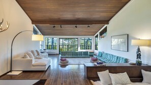 A modern living room with a wooden ceiling, large windows, and a mix of seating arrangements.