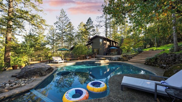 A swimming pool with lounge chairs and inflatable rings, surrounded by trees and a wooden deck. - 10-acre Wellness Retreat, Pool, Sauna, Ceremony Tent Fable Sonoma by Avantstay (Santa Rosa)