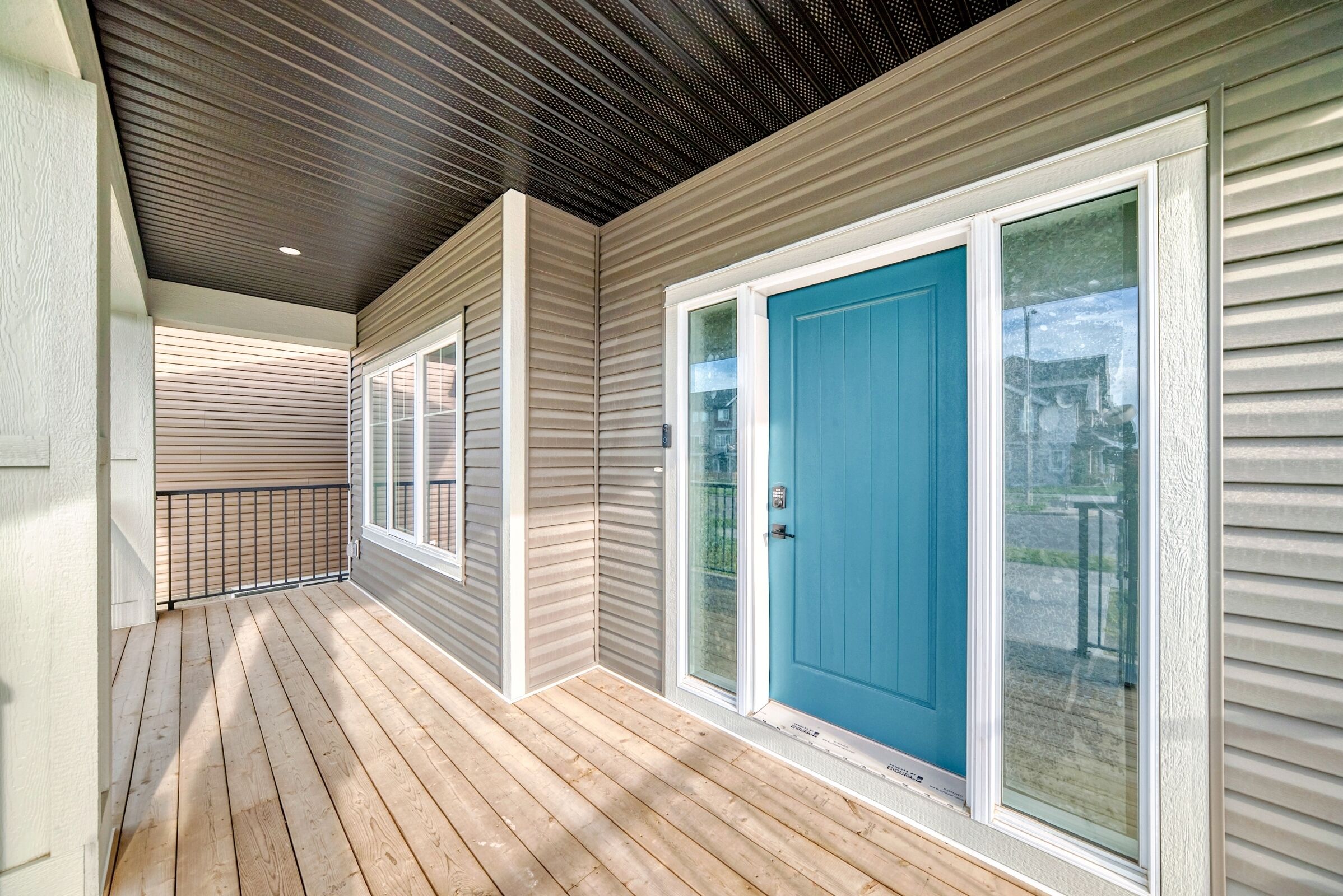 A covered porch with a wooden deck, a blue door, and a metal railing.