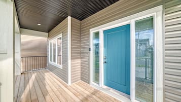 A covered porch with a wooden deck, a blue door, and a metal railing.
