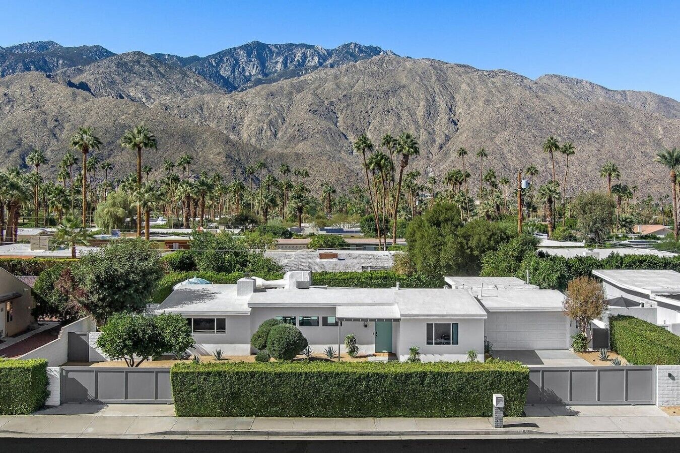 A residential area with modern houses, palm trees, and mountains in the background.