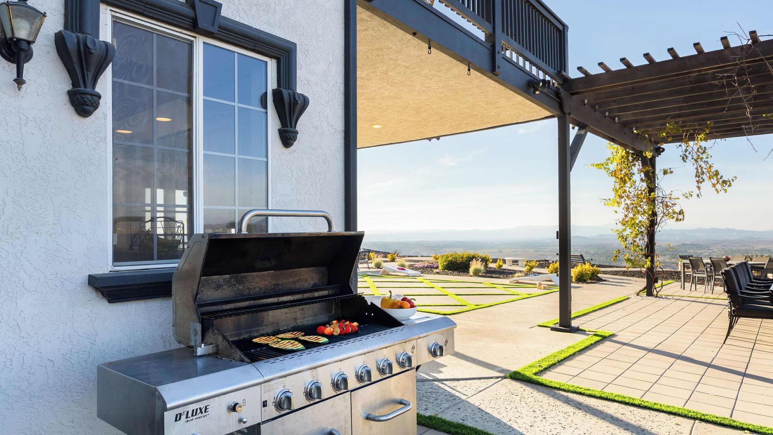 An outdoor grill with a view of a landscaped garden and distant mountains.
