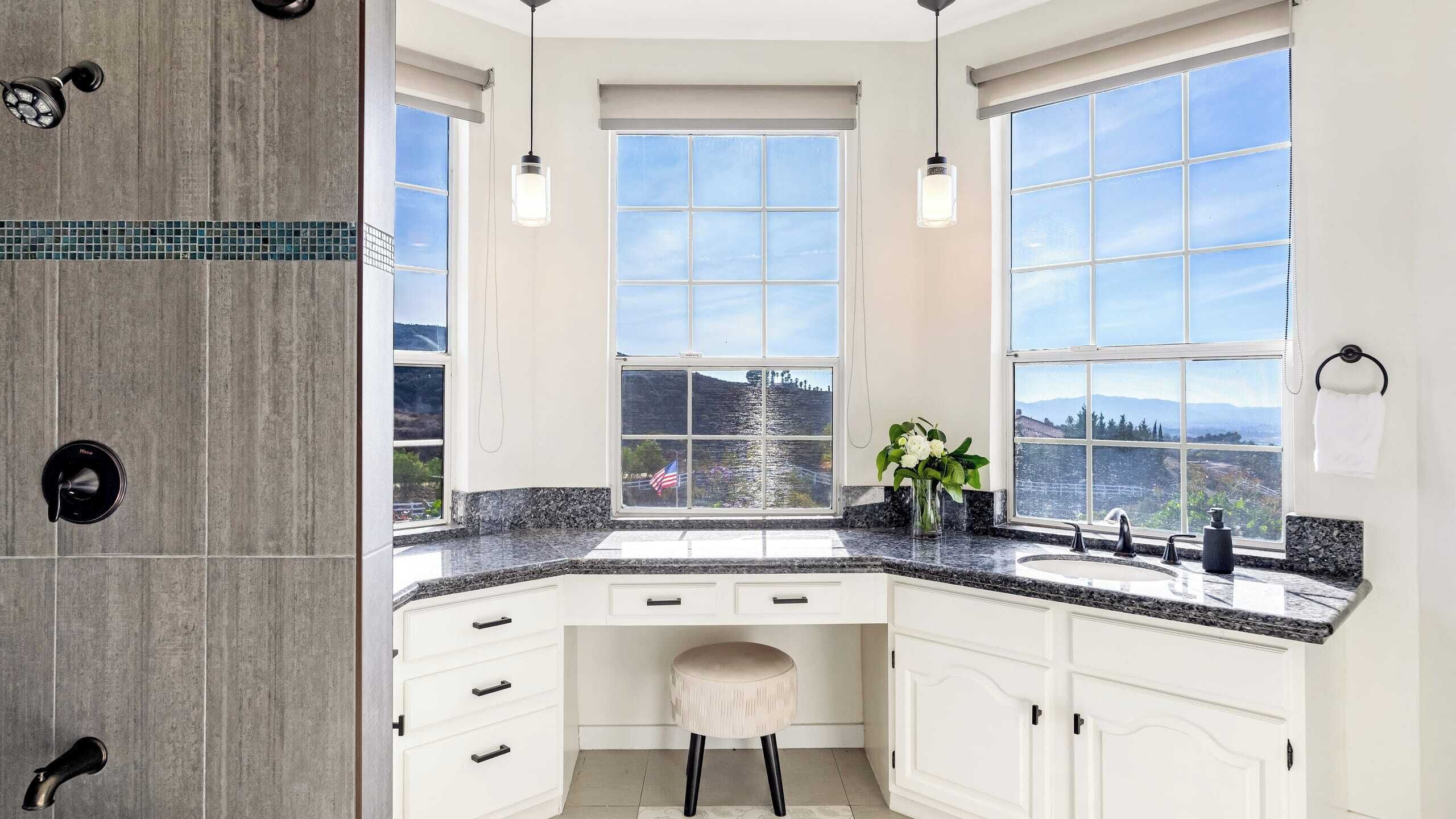 A modern kitchen with white cabinetry, granite countertops, and large windows offering a scenic view.
