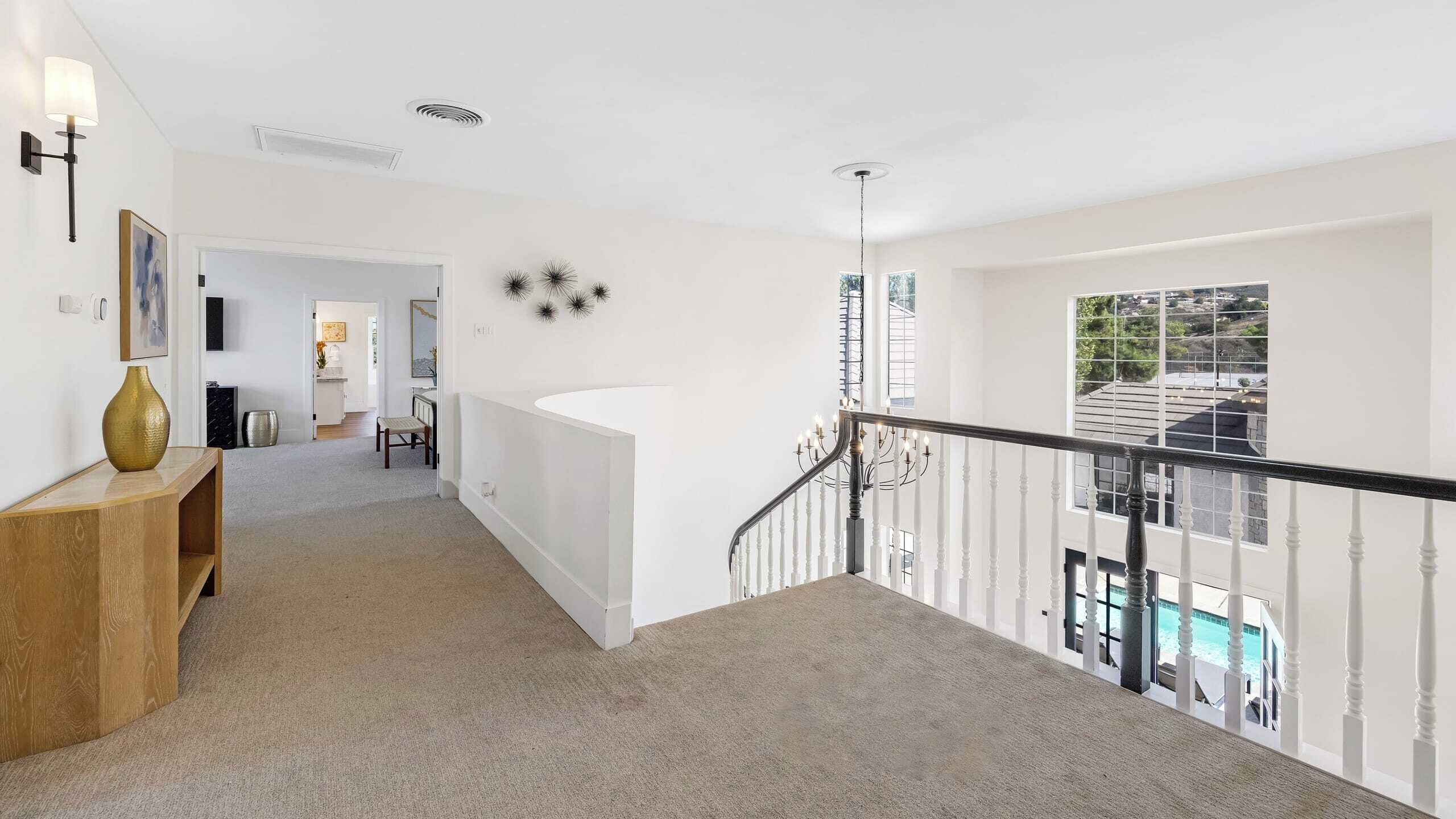 A spacious hallway with a white staircase leading to a balcony with a pool view.